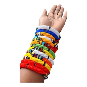 May include: A collection of beaded bracelets in various colors, including red, yellow, green, and blue. The bracelets are stacked on a wrist, showcasing the vibrant and detailed beadwork. The bracelets appear to be handmade.