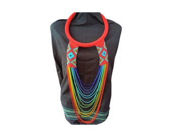 May include: A vibrant beaded necklace with a red collar and geometric patterns in turquoise, red, and yellow. The necklace features multiple strands of colorful beads, transitioning from red to yellow, creating a rainbow effect. The necklace is displayed on a dark gray background.