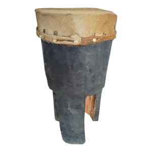 May include: A handcrafted drum with a light brown, stretched hide drumhead. The drum's body is dark grey, with a flared shape and a wooden base. The drum is likely used for musical performances.