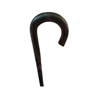 Può includere: Un bastone di legno marrone scuro con un manico curvo. Il bastone ha una finitura liscia con venature del legno visibili e intagli decorativi vicino alla parte superiore del fusto. L'impugnatura è curva per una presa comoda.
