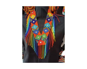 May include: A vibrant, beaded necklace with a V-shaped design. The necklace features a pattern of colorful squares in orange, blue, green, and white. Long strands of beads in rainbow colors hang from the bottom, creating a striking visual effect. The necklace is worn over a black garment.