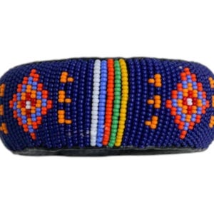 Puede incluir: Una pulsera de cuentas azul con un patrón geométrico en naranja, rojo y blanco. El centro presenta rayas verticales de cuentas blancas, verdes, amarillas y naranjas. Este accesorio artesanal es único.