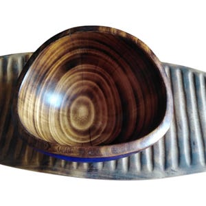 May include: A wooden bowl with a distinctive grain pattern, featuring shades of brown. The bowl has a blue accent at the base and is set on a textured, ridged wooden surface. The bowl's interior is smooth and polished.
