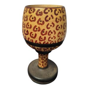Puede incluir: Un cáliz decorativo con un diseño único. El cáliz presenta una base y un tallo de color marrón claro, con una base circular marrón oscuro. La copa es de color marrón claro con un patrón repetido de formas marrones oscuras.