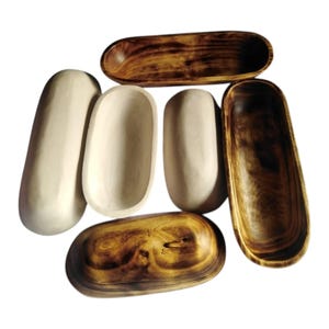 May include: An assortment of wooden serving bowls and trays in various shapes and colors. Some are light-colored, while others are a rich, dark brown. The bowls and trays are oval and rectangular, perfect for serving food or displaying items.