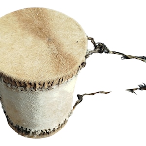 Pode incluir: Um pequeno tambor redondo de couro marrom com uma cabeça de pele branca e uma longa correia de couro marrom.
