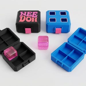 May include: Two square storage cases in black and blue, each featuring a pink latch and four internal compartments. The black case displays the text "NEE DOH" in pink. Two translucent pink dice with "NEE DOH" text are included with the cases.