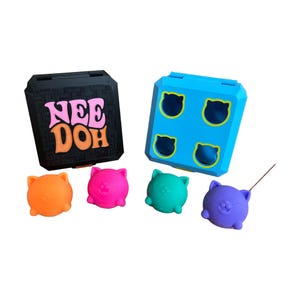 May include: A black square case with the pink and orange text NEE DOH, a blue square case with four cat-shaped cutouts, and four small spherical cat-shaped toys in orange, pink, teal, and purple colors arranged in front of the cases.