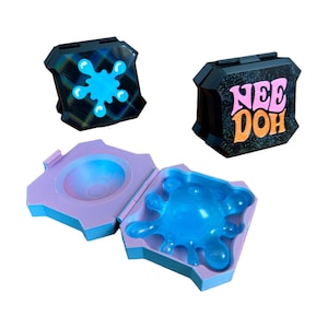 May include: Two black square cases with hinged lids, one featuring a blue splatter graphic and the other displaying the text "NEE DOH" in pink and orange. A third open light blue case reveals a translucent blue splat-shaped toy inside.