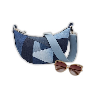 Könnte beinhalten: Eine Schultertasche aus Jeans-Patchwork mit hellblauem Riemen und goldfarbener Hardware. Neben der Tasche befindet sich eine goldgerahmte Sonnenbrille mit braunen Gläsern. Die Tasche hat eine Halbmondform.