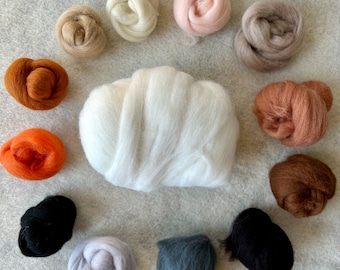 May include: A large central bundle of white wool roving surrounded by twelve smaller, circular bundles of wool in various colors including cream, light pink, beige, orange, rust, brown, black, grey, and charcoal, all arranged in a circular pattern.