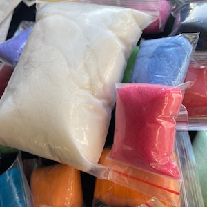 May include: A collection of assorted craft supplies consisting of multiple clear plastic resealable bags filled with loose, soft, fibrous material in various solid colors including white, bright pink, orange, blue, and purple.