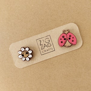 May include: A set of two wooden buttons featuring a ladybug and a daisy. The ladybug is red with black spots and the daisy is white with a brown center. The buttons are on a card with the text "Zig Zag Crafts".