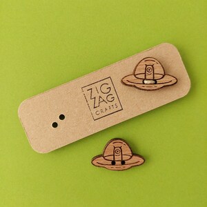 May include: Two wooden UFO buttons with a brown finish. The buttons are on a brown card with the text "Zig Zag Crafts".