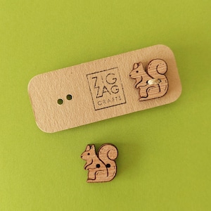 May include: Two wooden buttons shaped like squirrels. The buttons are brown and have a natural wood finish. The buttons are on a brown card with the text "Zig Zag Crafts" printed on it.