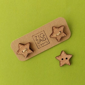 Könnte beinhalten: Drei sternförmige Holzknöpfe mit natürlicher Holzoptik. Die Knöpfe befinden sich auf einer braunen Karte mit dem Text "Zig Zag Crafts".