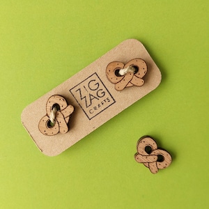 May include: Three wooden buttons shaped like pretzels. The buttons are on a brown card with the text "Zig Zag Crafts".