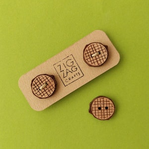 May include: Three wooden buttons with a grid pattern. The buttons are brown with a natural wood finish. The buttons are on a brown card with the text "Zig Zag Crafts".