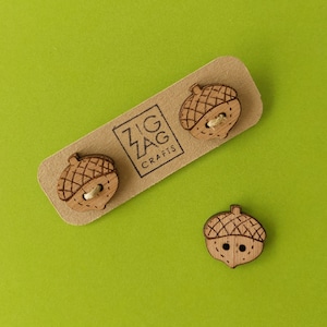 Könnte beinhalten: Drei braune Holz-Eichelknöpfe. Die Knöpfe befinden sich auf einer Karte mit dem Text "Zig Zag Crafts".