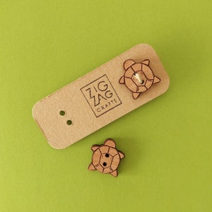May include: Two wooden turtle buttons with a brown wood finish. The buttons are on a brown card with the text "Zig Zag Crafts".