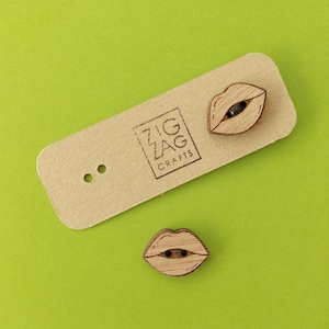 May include: Two wooden buttons shaped like lips with a black button in the center. The buttons are on a brown card with the text "Zig Zag Crafts" printed on it.