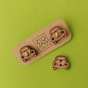 Könnte beinhalten: Drei Holz-Knöpfe in Form von Vintage Volkswagen Käfern. Die Knöpfe sind braun und haben einen weißen Umriss. Die Knöpfe befinden sich auf einer Holzkärtchen mit dem Text "Zig Zag Crafts".