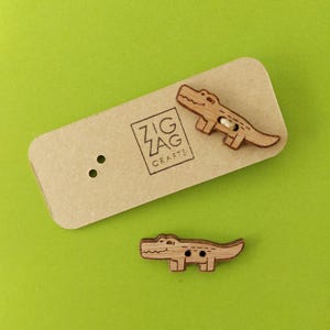 May include: Two wooden alligator buttons with a brown wood finish. The buttons are on a brown paper background with the text "Zig Zag Crafts".