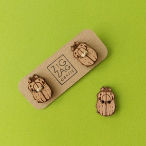 Puede incluir: Tres botones de escarabajo de madera con un acabado de madera natural. Los botones están en una tarjeta marrón con el texto "Zig Zag Crafts".