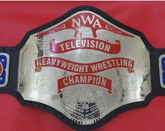 Op de afbeelding: Een zilveren en zwarte NWA Television Heavyweight Wrestling Champion-riem. De riem heeft een grote zilveren middenplaat met rode letters en een zwarte leren band. De riem heeft twee zijplaten met een rood en blauw ontwerp.