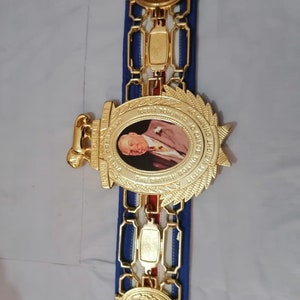 May include: A gold boxing championship belt with a blue and red strap. The belt features a large oval medallion with a portrait of a man and the text "THE BRITISH BOXING BOARD OF CONTROL LIGHTWEIGHT CHAMPION 1969/1974".