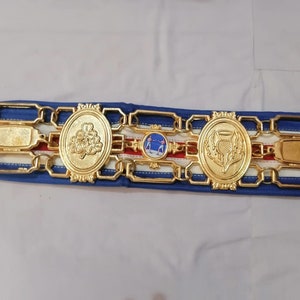 May include: A gold belt with a blue and white ribbon. The belt has three oval medallions with different designs. The medallions feature a clover, a thistle, and a scene of two people fencing.
