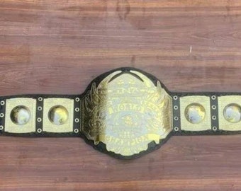 Op de afbeelding: Een gouden en zwarte worstelgordel met een groot, versierd middenstuk met een gevederde adelaar en de woorden "World Heavyweight Championship".