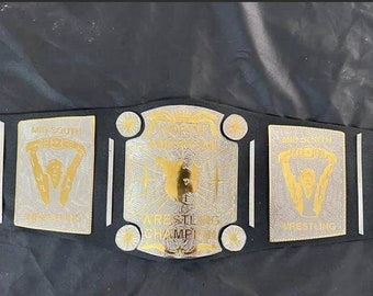 May include: A black and gold wrestling championship belt with the words "Mid-South Wrestling" and "Wrestling Champion" on it.