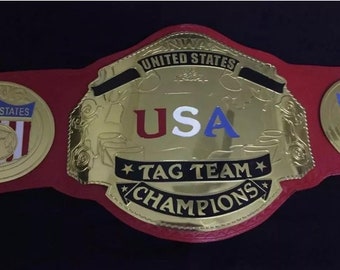 Op de afbeelding: Een gouden worstelkampioensgordel met een rode band. De middelste plaat heeft een gouden USA-ontwerp met rode, witte en blauwe letters. De riem heeft ook twee kleinere platen met de woorden "United States" en een rood-wit-blauw Amerikaans vlagontwerp.