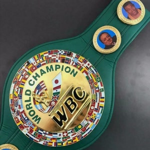 Może przedstawiać: Zielony sk&oacute;rzany pas mistrzowski World Boxing Council (WBC) z złotymi akcentami. Pas posiada dużą okrągłą płytę centralną z logo WBC i napisem "Mistrz Świata" złotymi literami. Płyta centralna jest otoczona pierścieniem flag reprezentujących r&oacute;żne kraje. Pas posiada r&oacute;wnież dwie mniejsze okrągłe płyty z portretami bokser&oacute;w.