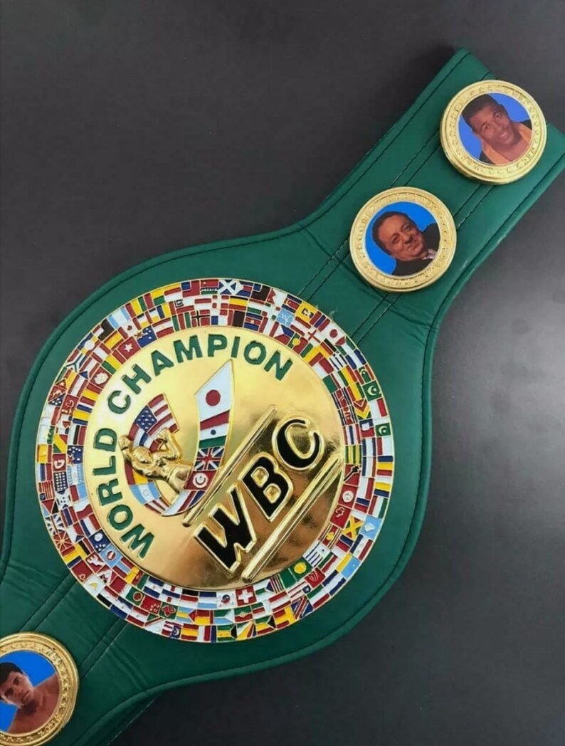 Może przedstawiać: Zielony sk&oacute;rzany pas mistrzowski World Boxing Council (WBC) z złotymi akcentami. Pas posiada dużą okrągłą płytę centralną z logo WBC i napisem "Mistrz Świata" złotymi literami. Płyta centralna jest otoczona pierścieniem flag reprezentujących r&oacute;żne kraje. Pas posiada r&oacute;wnież dwie mniejsze okrągłe płyty z portretami bokser&oacute;w.