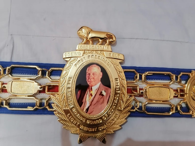 May include: A gold boxing belt with a large, ornate center plate featuring a portrait of a man and the text "Lord Lonsdale Boxing Belt First President The British Boxing Board of Control (1929) Light Weight Champion".