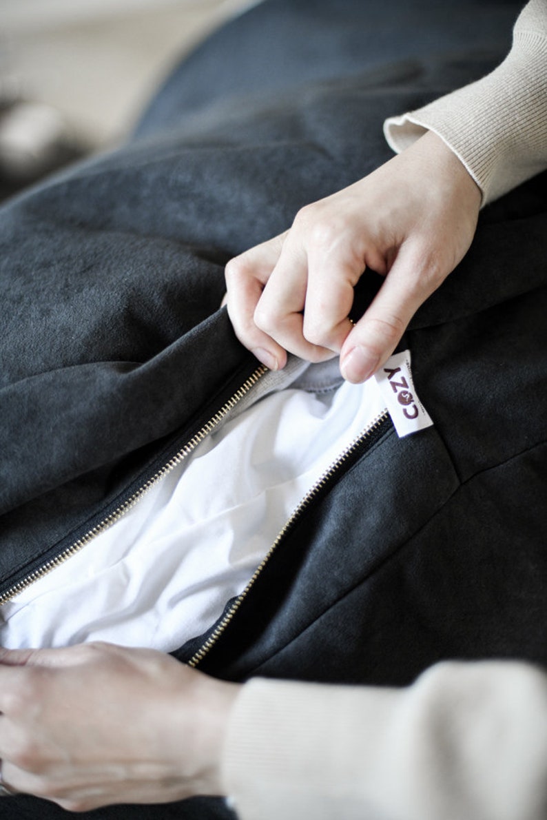 May include: Close-up of a dark gray beanbag chair with a gold zipper. The zipper is partially open, revealing a white interior. A small tag with the word "COZY" is attached to the beanbag.