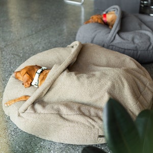 Pu&ograve; includere: Due cani riposano in comode cucce rotonde. Uno &egrave; in una cuccia beige, parzialmente coperto da una coperta abbinata. L'altro &egrave; in una cuccia grigia. Entrambi i cani sono marroni con collari.