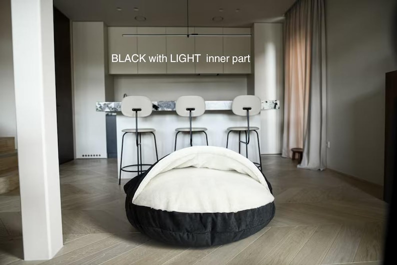 May include: A black and white pet bed with the text "BLACK with LIGHT inner part". The bed has a round shape with a black exterior and a white, cushioned interior. The bed is in a modern room setting.