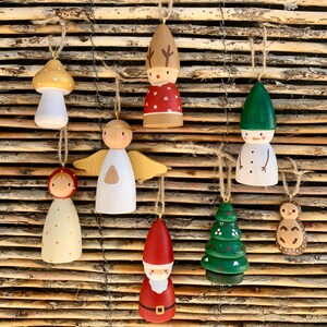 Peut inclure: Collection de neuf ornements de Noël en bois suspendus devant un fond en bois rustique. Les ornements comprennent un champignon, un renne, un bonhomme de neige, un ange, un Père Noël, un sapin de Noël, un hérisson et une figurine. Chaque ornement est peint avec des couleurs vives.