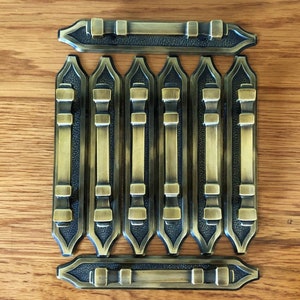 May include: Set of eight antique gold cabinet door pulls with a black finish. The pulls have a rectangular shape with a pointed top and bottom.