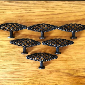 May include: A set of six black cabinet knobs, each featuring a horizontal, elongated, cage-like design formed by intersecting metal wires. The knobs are arranged in a triangular formation, with each piece supported by a single central post base.