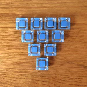 May include: A triangular arrangement of 10 small, square, light blue tiles with a clear, slightly frosted finish.