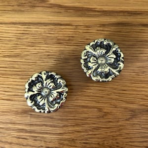 May include: Two ornate brass drawer pulls with a floral design.