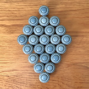 May include: A collection of 20 blue ceramic knobs with a decorative floral design. The knobs are arranged in a diamond shape on a wooden surface.