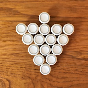 May include: A white arrow shape made of 15 white plastic bottle caps with a gray ring around the edge. The caps are arranged in a triangular shape with the point of the arrow pointing down.