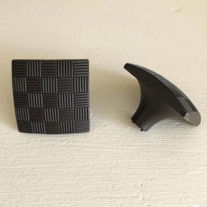 May include: Two dark brown shoe heels and a square shoe sole. The sole has a woven pattern. The heel has a curved design with a ridged pattern. The objects are on a light-colored surface.