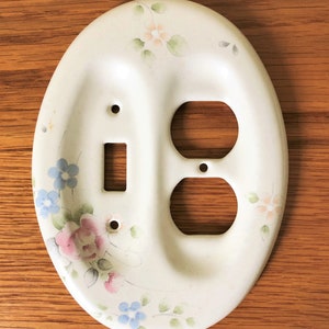 May include: White ceramic light switch and outlet cover with a floral design in shades of pink, blue, and green.
