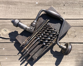 May include: A vintage hand drill with a wooden handle and a set of drill bits. The drill bits are arranged in a fan shape on a wooden surface.